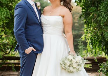 Bride and groom smiling under lush greenery on their wedding day.
