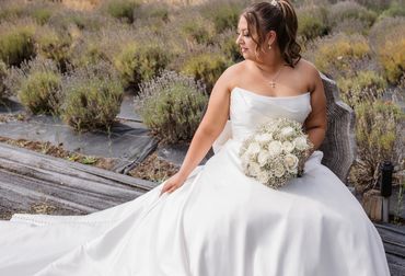 Bride in a white gown holding a bouquet, sitting in a lavender field.