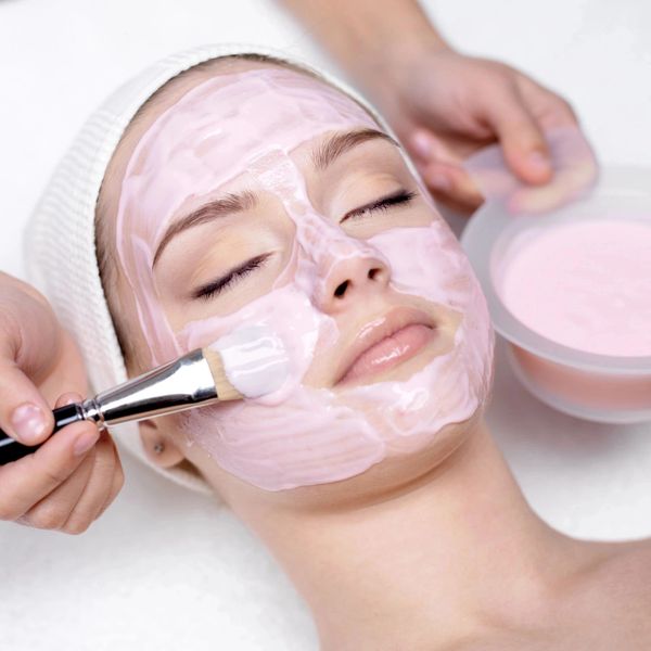 Woman getting relaxing facial and pink mask application by esthetician