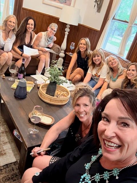 Group of women smiling and sitting around a coffee table with drinks and papers.