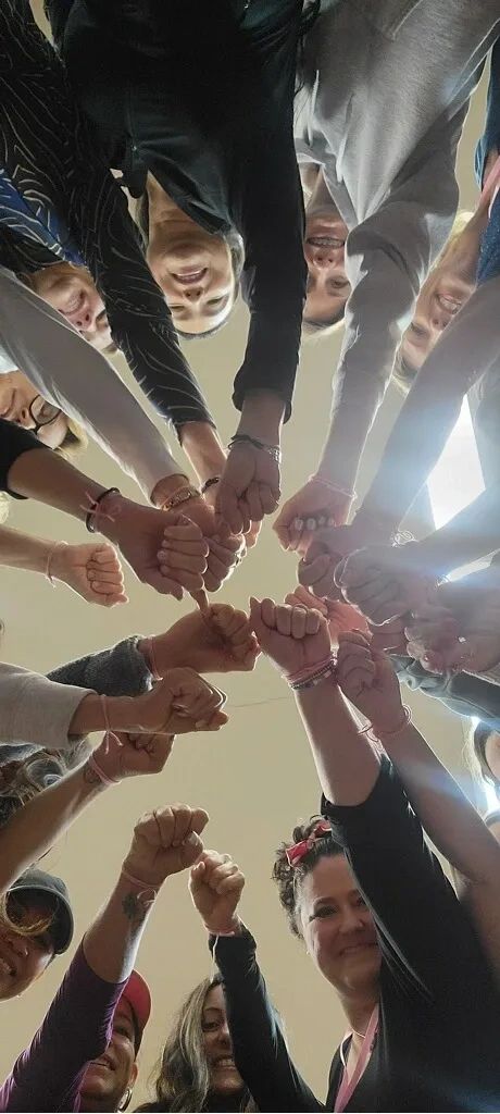 A group of people standing in a circle with fists joined together in the center.