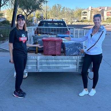 Two women standing by a trailer loaded with bins and boxes.