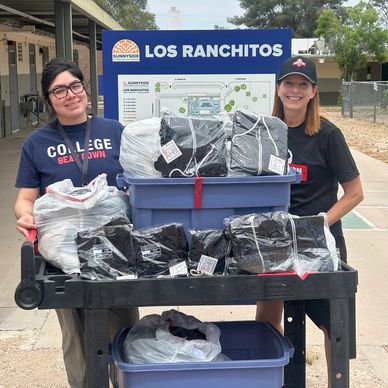 Two women smiling with donation bags and bins at Los Ranchitos.