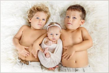Three shirtless kids lying on a white furry surface.