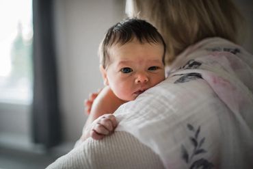 Baby resting on adult's shoulder indoors.