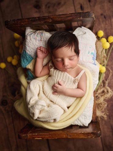 Sleeping newborn baby in a knitted outfit on a vintage chair.
