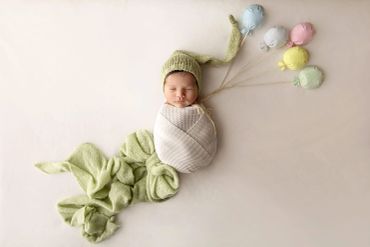 Newborn baby wrapped with knitted balloons and hat.