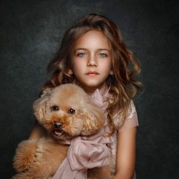 Young girl holding a fluffy dog with a large bow.