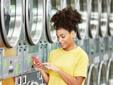 Woman starting laundry machines with her phone using the Huebsch app at Mary’s Laundromart.
