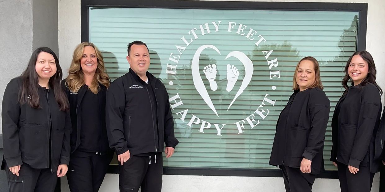 A group of five smiling professionals standing in front of a podiatry clinic window.
