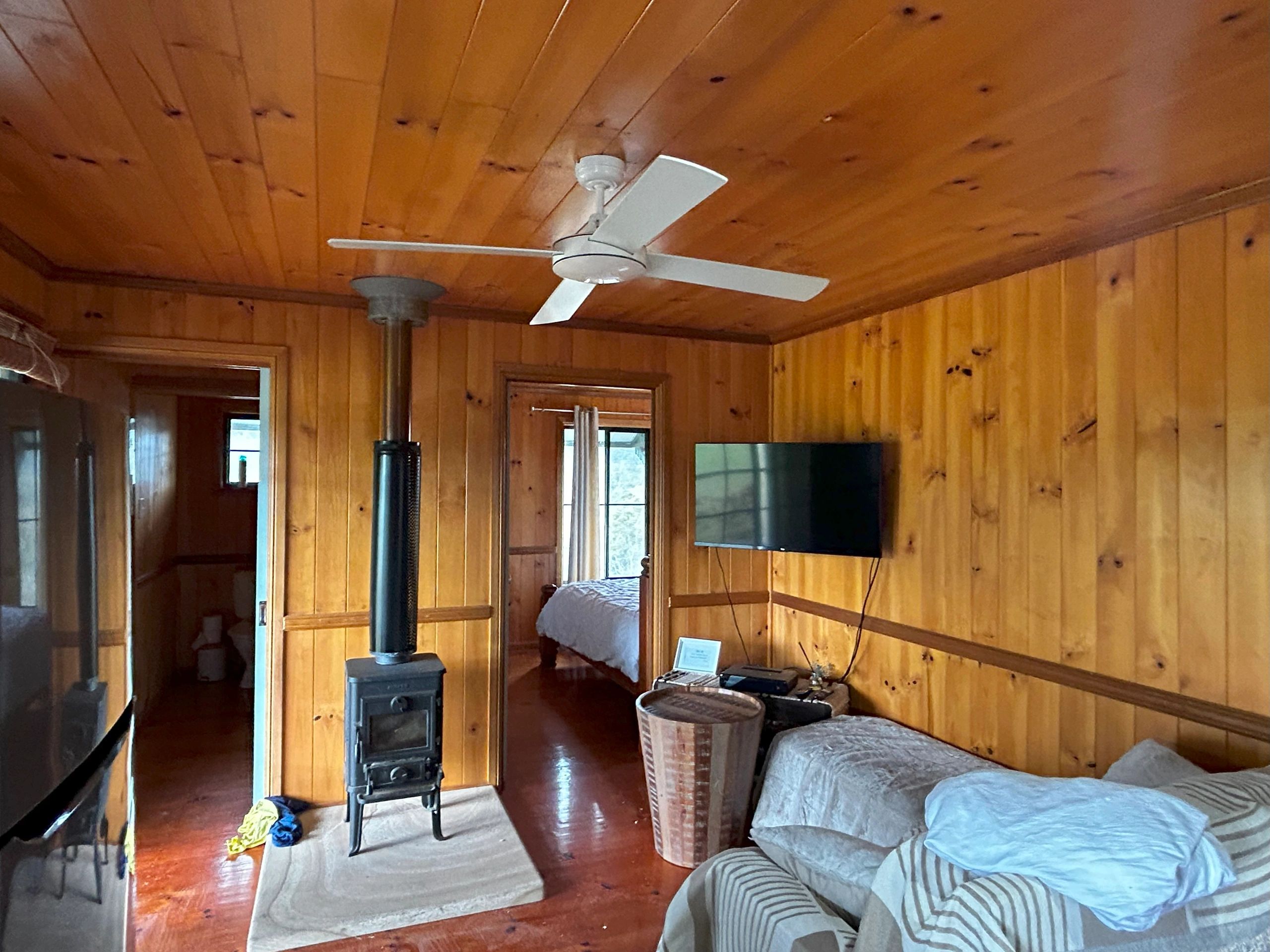 Cozy wooden room with a ceiling fan, wood stove, and TV.