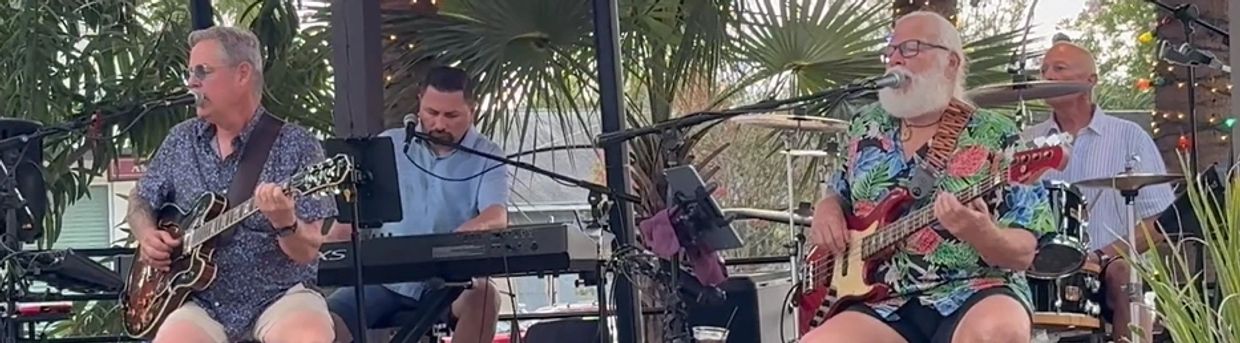 Band performing live outdoors with guitar, keyboard, bass, and drums.