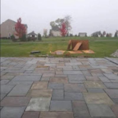 A backyard with a stone patio and a wooden ramp on the grass.