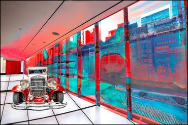 Vintage car displayed in a modern, colorful glass-walled showroom.