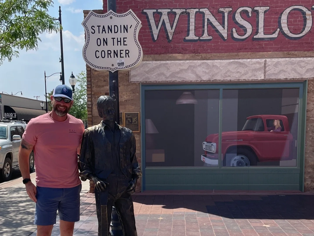 Man posing with a statue at the 'Standin' on the Corner' in Winslow.