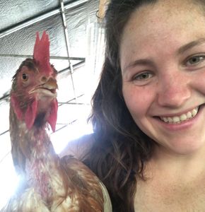A woman smiling next to a chicken inside a barn.