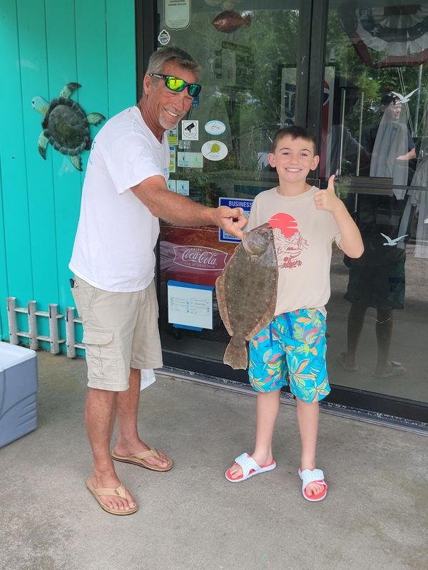 A man and boy proudly display a flatfish outside a store.