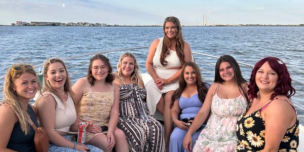 A group of eight women smiling by the waterfront during daytime.