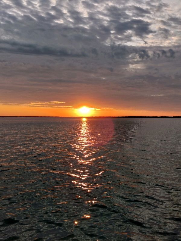Sunset over a calm body of water with dramatic clouds.