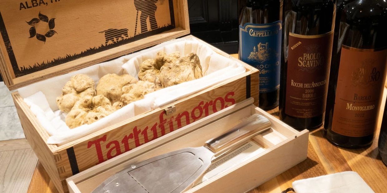 Box of white truffles with a truffle slicer and wine bottles.