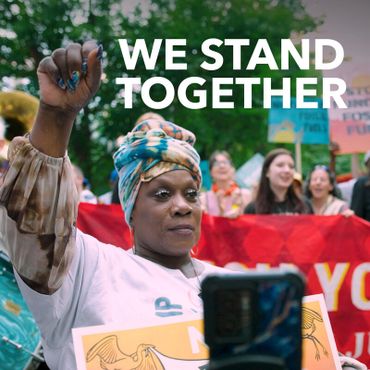 A determined person raising a fist at a protest with 'WE STAND TOGETHER' text.