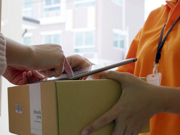 Person signing on a tablet while receiving a package from a delivery worker.