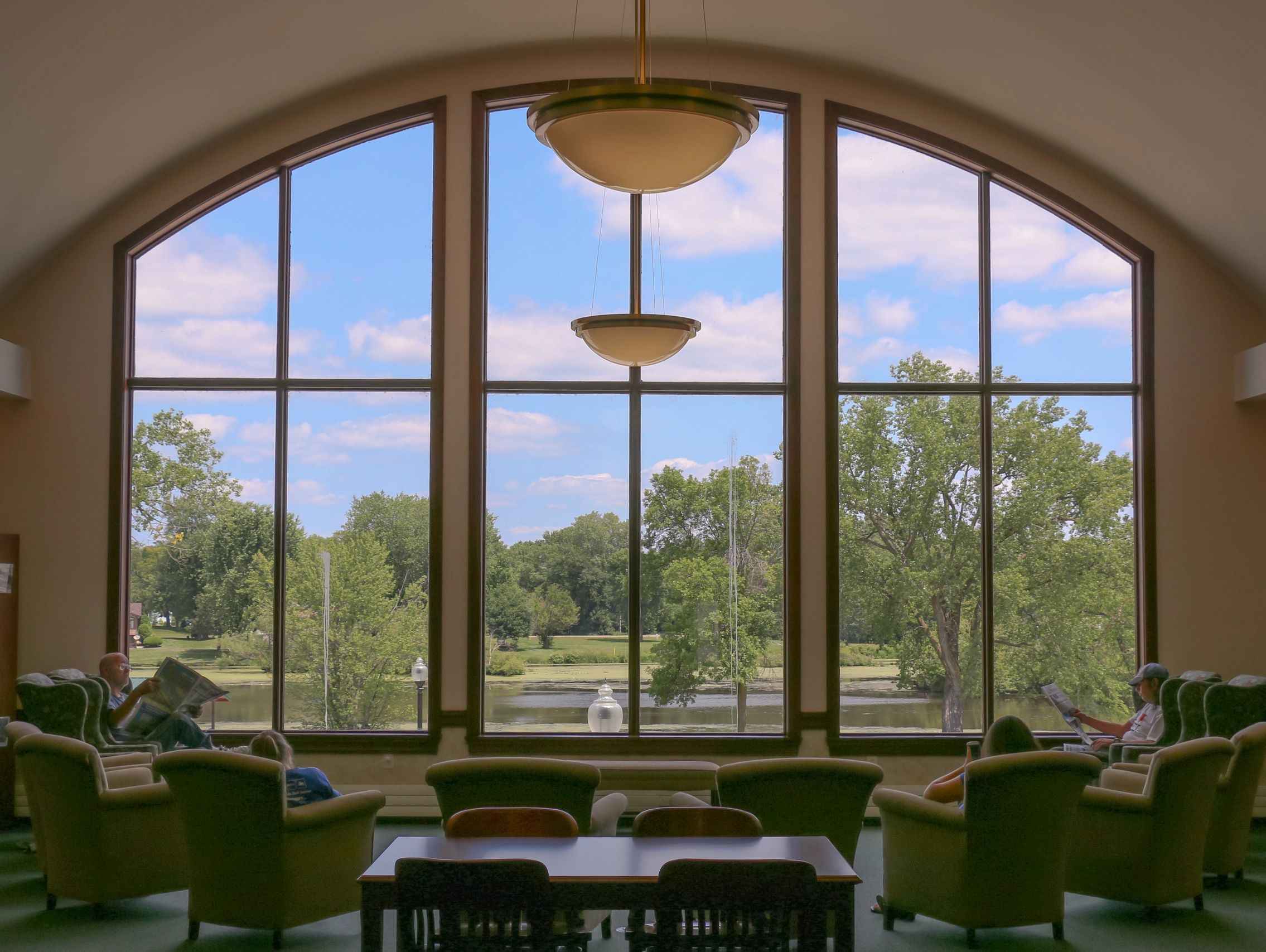 Four people reading in armchairs in front of big windows overlooking trees and the Lemonweir River.