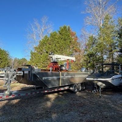A boat on a trailer parked outdoors with trees and a clear blue sky.