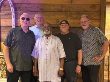 Five men smiling together inside a wooden room.