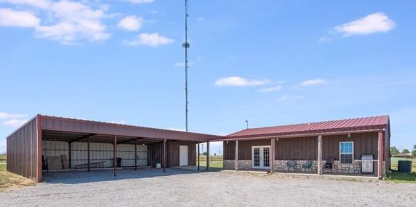 Open metal shed and building with red roofs under a blue sky.