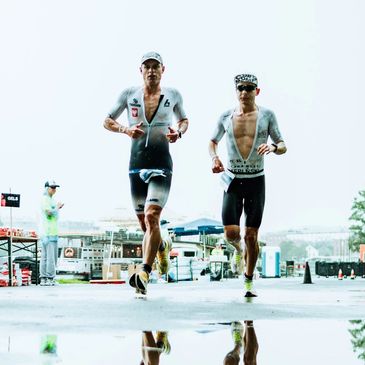 Two male athletes running in a race wearing sports gear and caps.