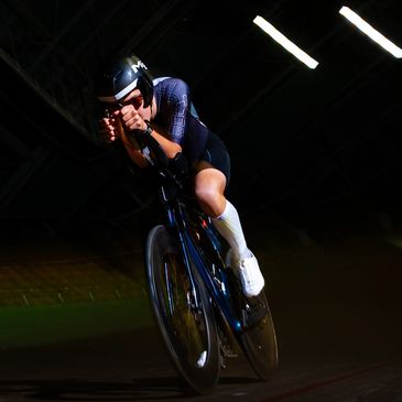 Cyclist racing intensely on a dark indoor track.