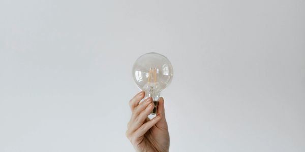 Hand holding a clear light bulb against a plain background.