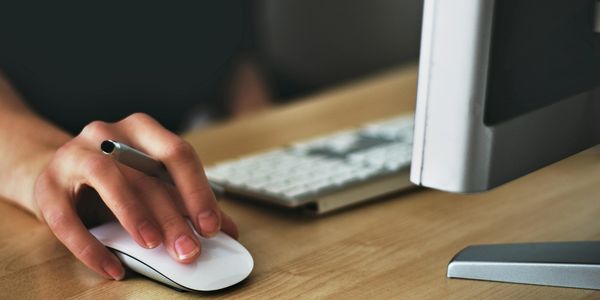 Hand using a white computer mouse next to a keyboard and monitor.