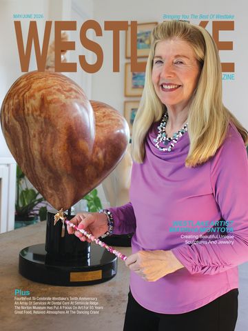 Woman smiling and holding a beaded necklace next to a wooden heart sculpture.