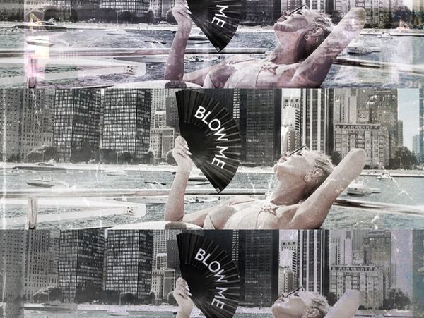 Woman relaxing by the water holding a fan that says 'BLOW ME'.