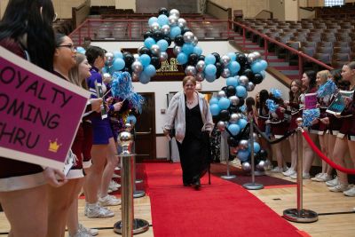 Woman walking on red carpet under balloon arch with cheering crowd.