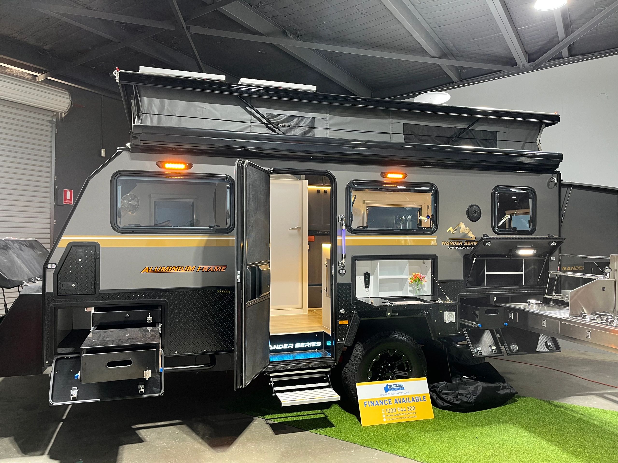 Modern off-road caravan with pop-up roof and outdoor kitchen setup.