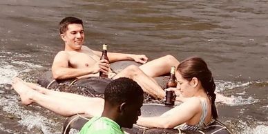 Three friends tubing on a river, enjoying drinks and sunny weather.