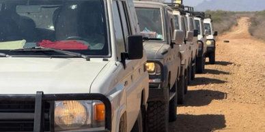 A convoy of off-road vehicles on a dirt path in a rugged landscape.