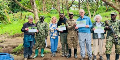Group of people holding certificates with soldiers in a forest setting.
