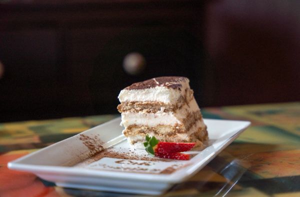 A slice of tiramisu with strawberries on a white plate.