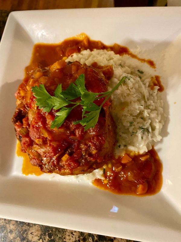 Chicken with tomato sauce served with creamy risotto on a white plate.