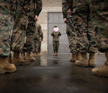 Military personnel standing in formation with one reading a document.