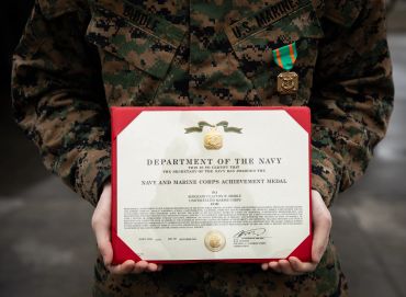 Marine in uniform holding a Navy and Marine Corps Achievement Medal certificate.