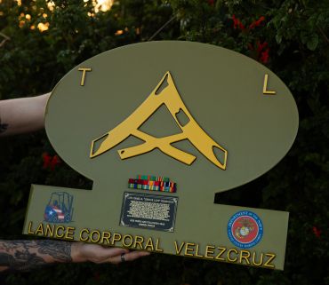 A military plaque honoring Lance Corporal Velezcruz with insignia and emblems.