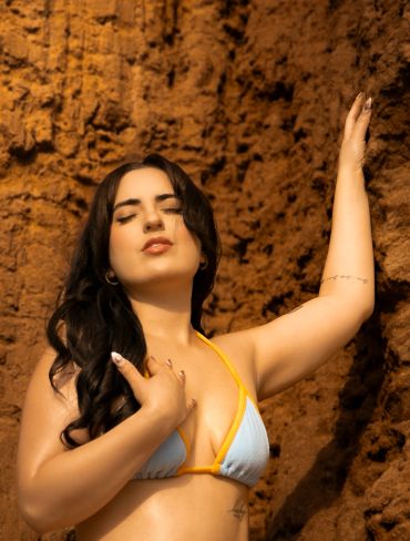 Woman in a bikini posing against a textured earthy background.