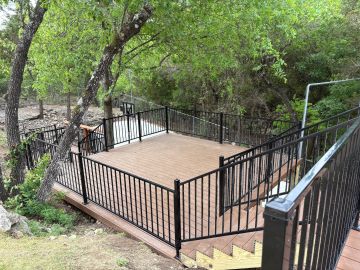 Spacious wooden deck with black metal railing surrounded by trees.