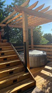Wooden deck with stairs, pergola, and an outdoor hot tub under clear blue sky.
