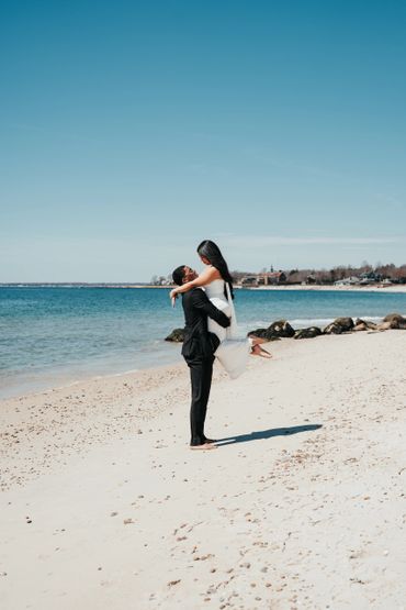 A groom lifts his bride on a sunny beach.